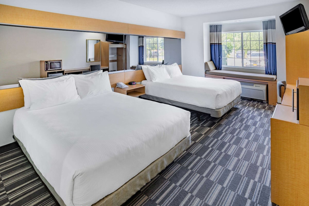 A hotel room with two beds, a television, a desk, and a window with curtains.