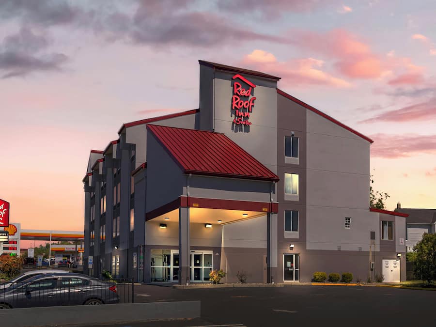 Punainen Red Roof Inn -hotelli, jossa on punainen katto, katettu sisäänkäynti ja taustalla näkyy Shell-huoltoasema.