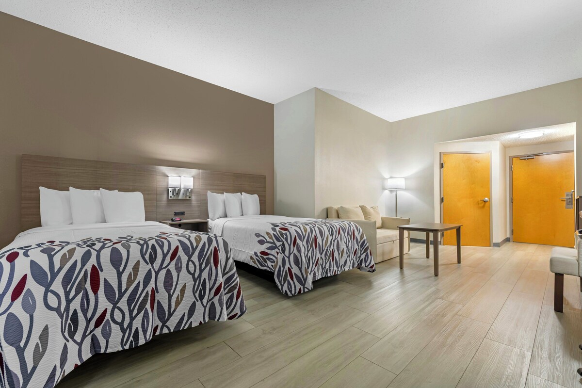 Une chambre d’hôtel avec deux lits, une petite table, une chaise et une porte.