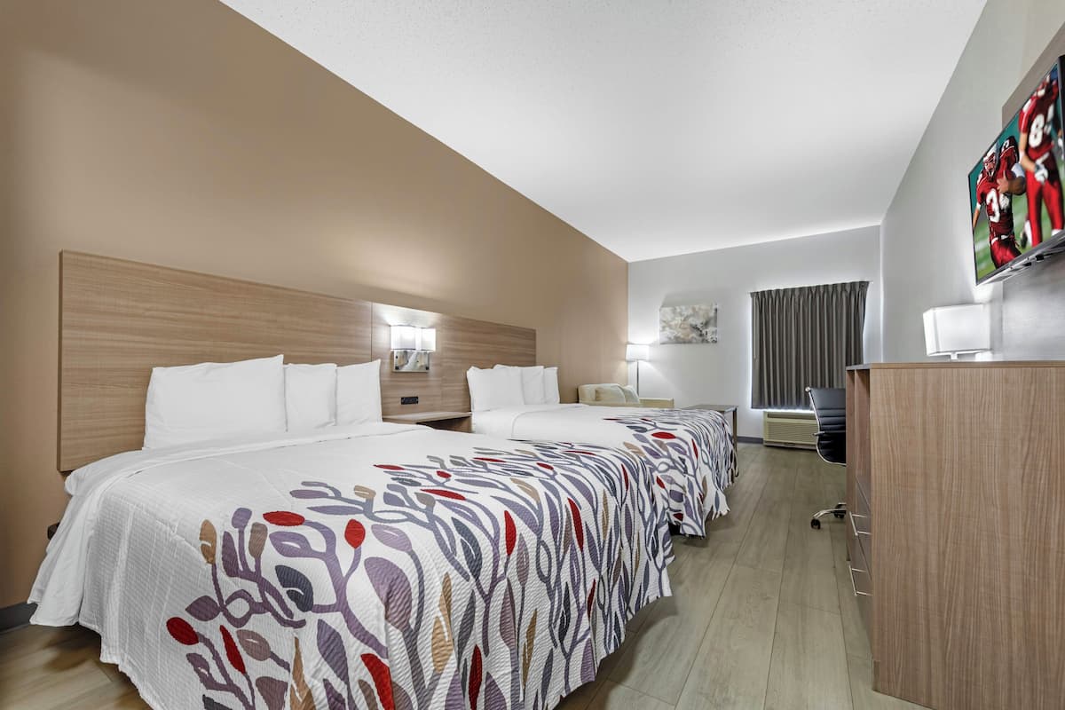 A hotel room with a large bed, a desk, a TV, and a window with curtains.
