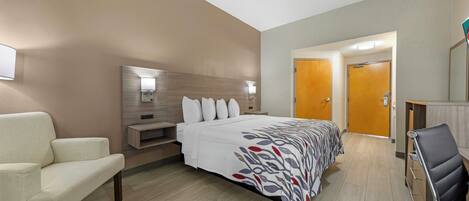 A hotel room with a bed, a chair, a desk, and a mirror.