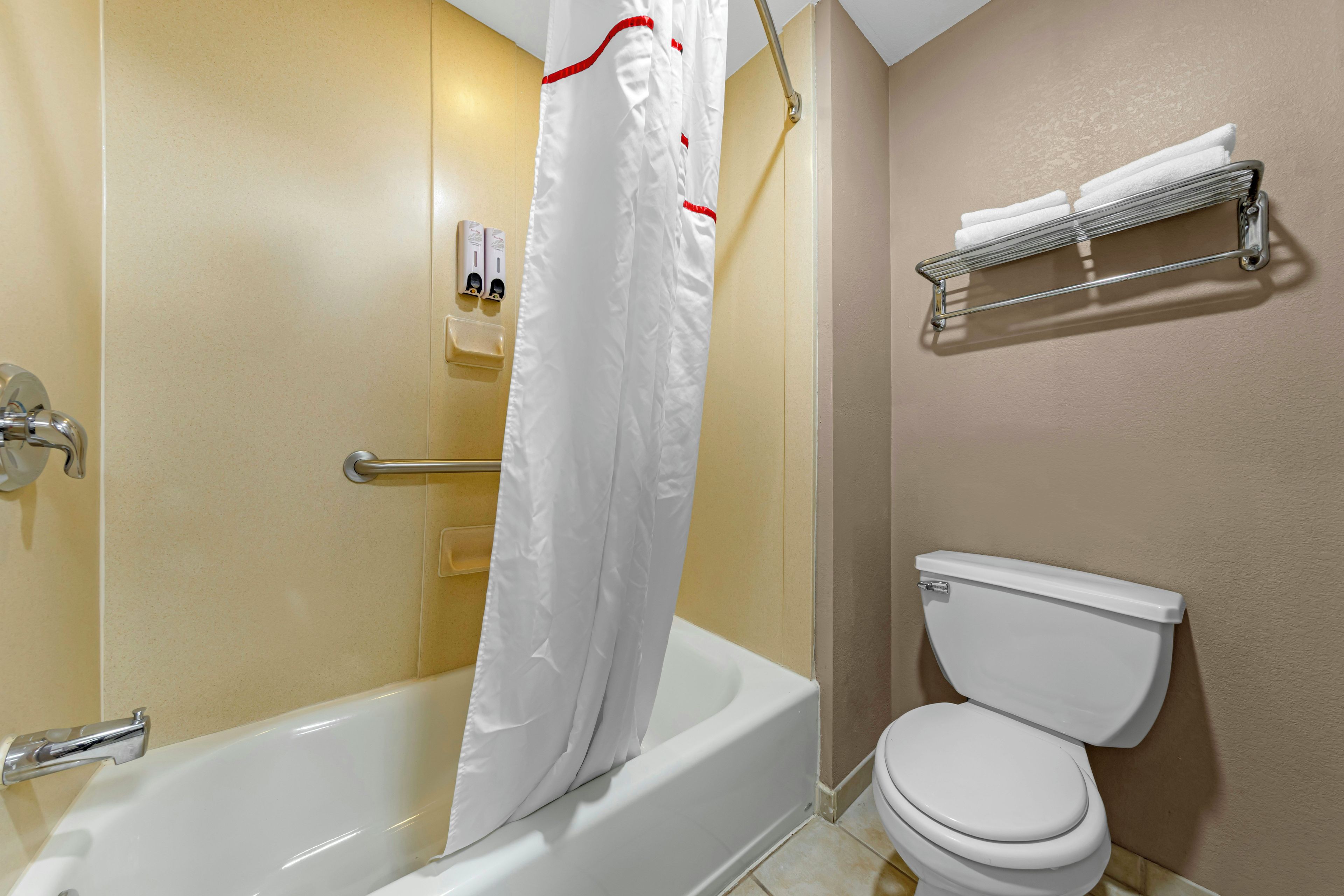 Un baño con bañera, inodoro, cortina de ducha y un perchero para toallas.