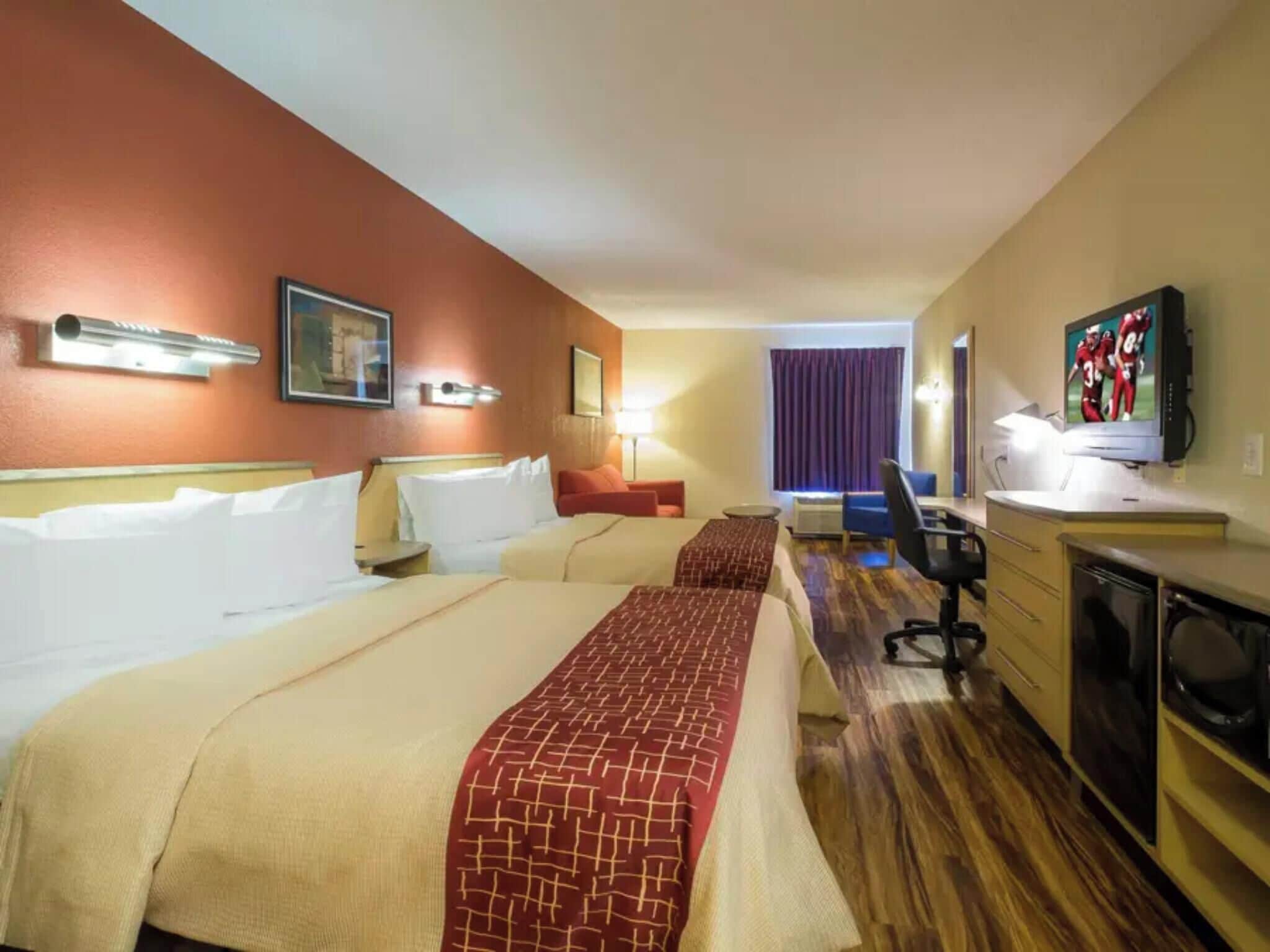 A hotel room with two beds, a desk, a chair, a television, and a window with curtains.
