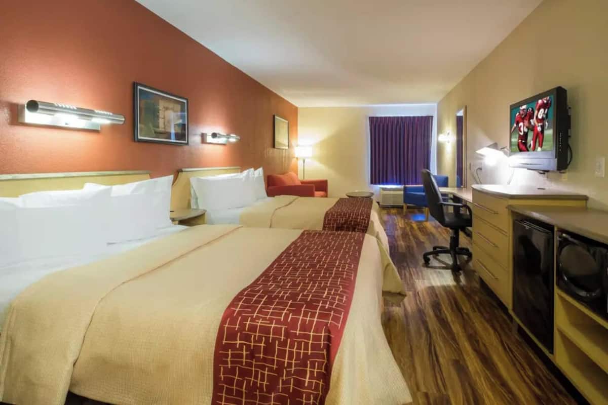 Une chambre d’hôtel avec deux lits, un bureau, une chaise, une télévision et une fenêtre avec des rideaux.