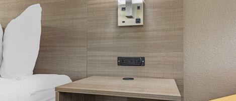 A hotel room with a bed, a bedside table with a power outlet, and a wall-mounted air conditioning unit.