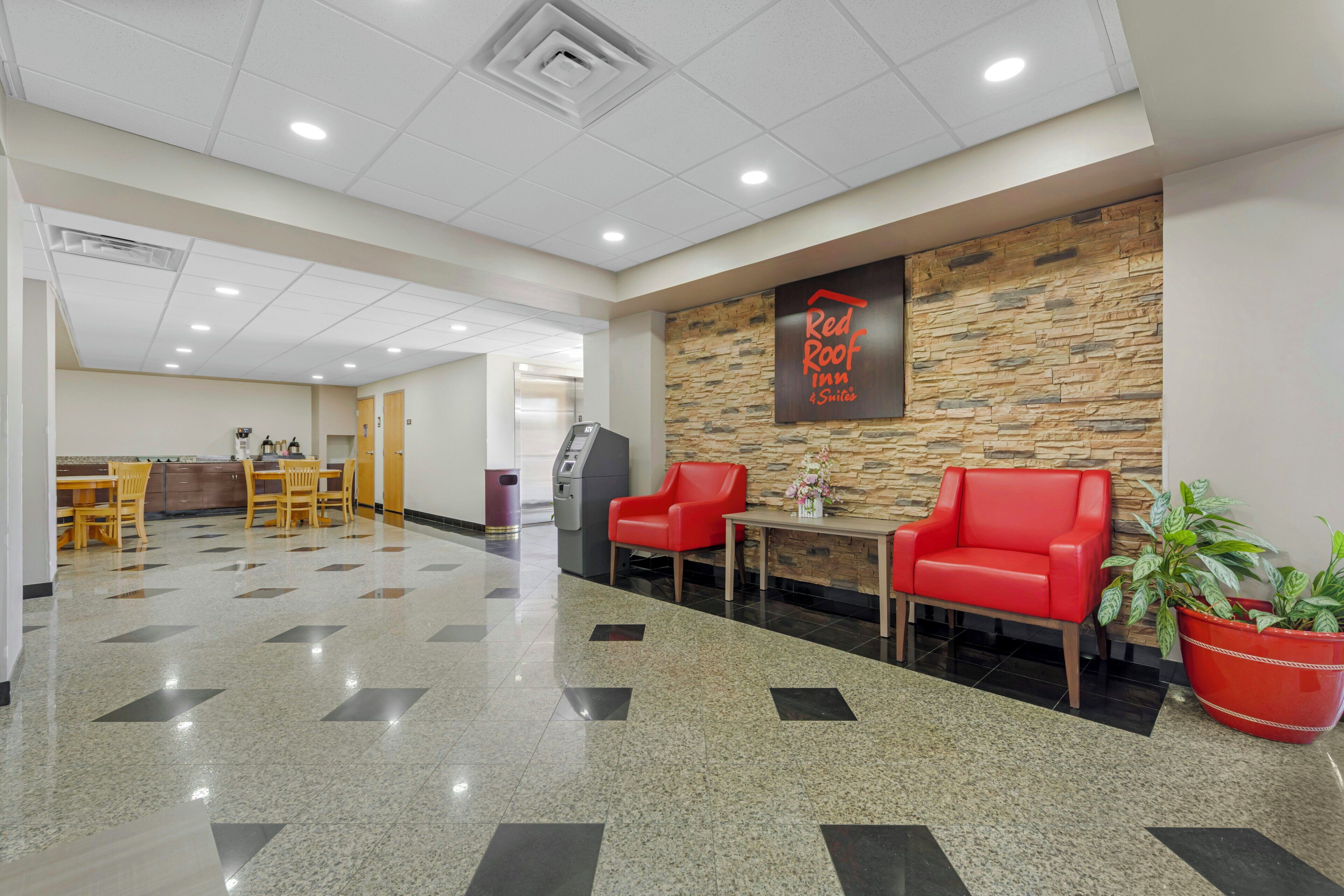 A hotel lobby with a stone wall, a Red Roof sign, a reception desk, and a self-service kiosk.