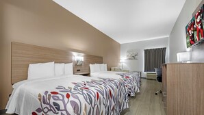 Una habitación de hotel con una cama grande, un escritorio, un televisor y una ventana con cortinas.