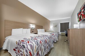 Ein Hotelzimmer mit einem großen Bett, einem Schreibtisch, einem Fernseher und einem Fenster mit Vorhängen.