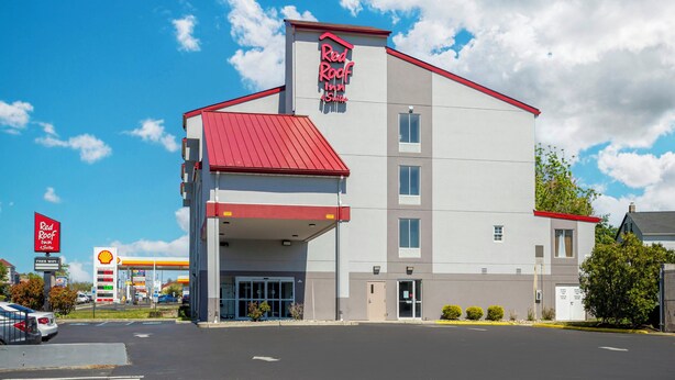 Un hotel Red Roof Inn con techo rojo y una estación de servicio Shell al fondo.