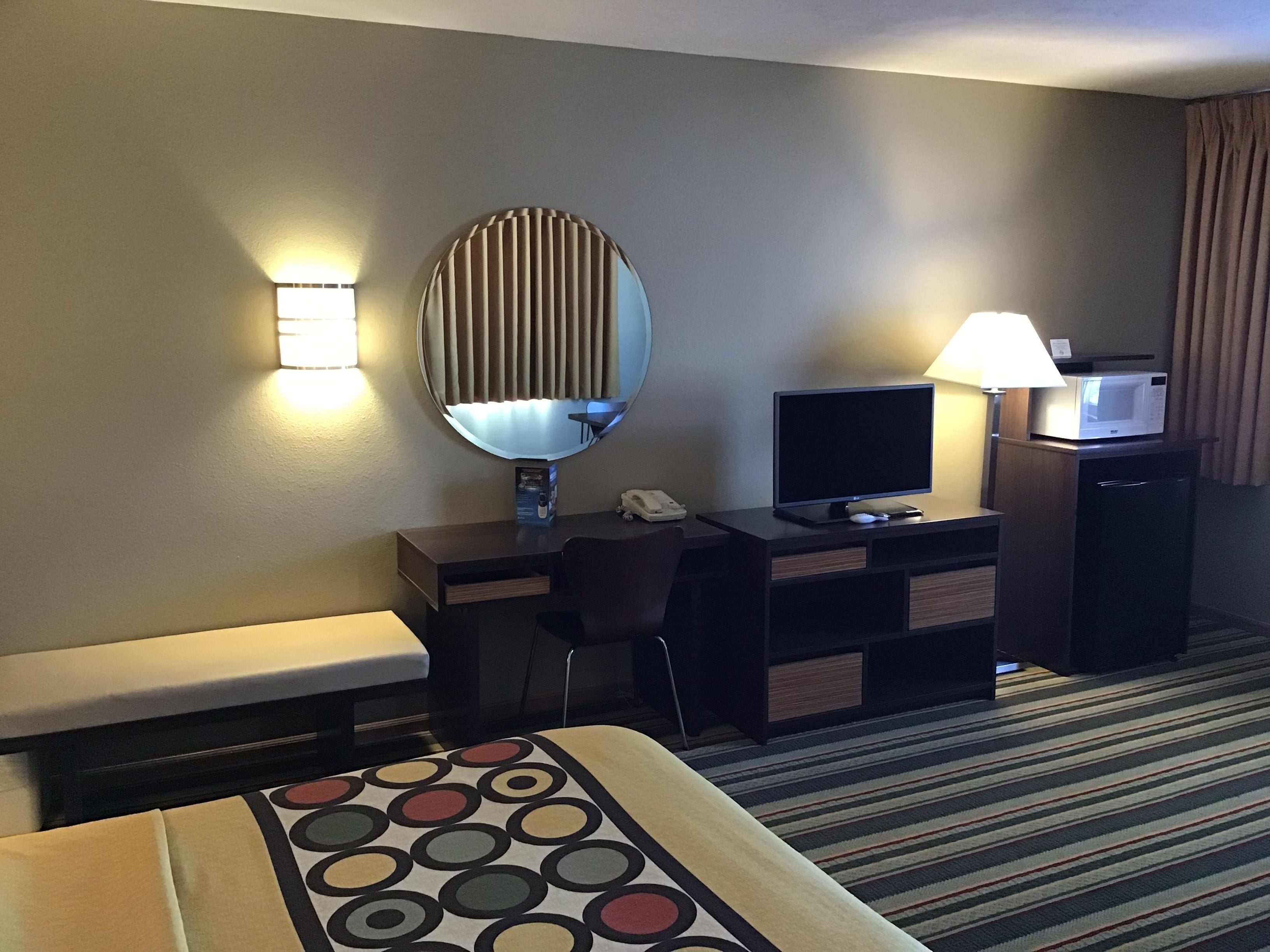 A hotel room with a bed, a desk with a computer, a TV, a microwave, and a lamp.