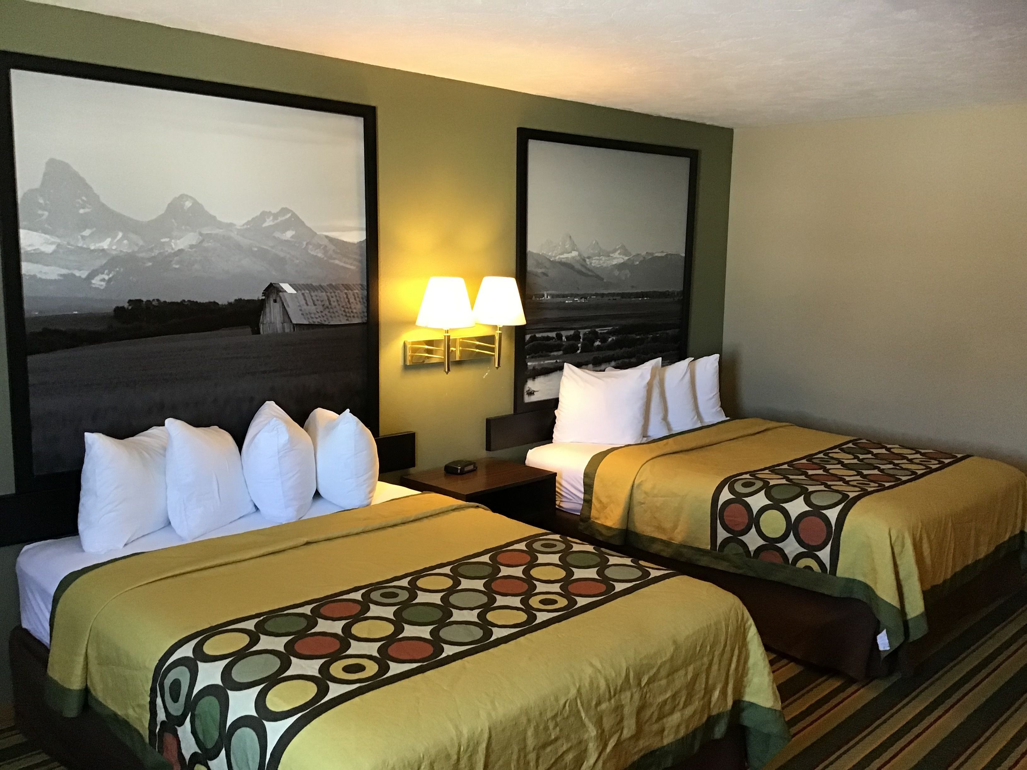 Habitación de hotel con dos camas, cada una con una colcha estampada y almohadas blancas. Hay dos lámparas de pared en la mesita de noche entre las camas.