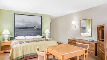 A hotel room with a bed, bedside tables, a desk, a chair, a lamp, a mirror, and a painting of mountains.