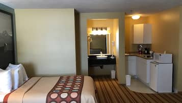Quarto de hotel com cama, banheiro e cozinha compacta.