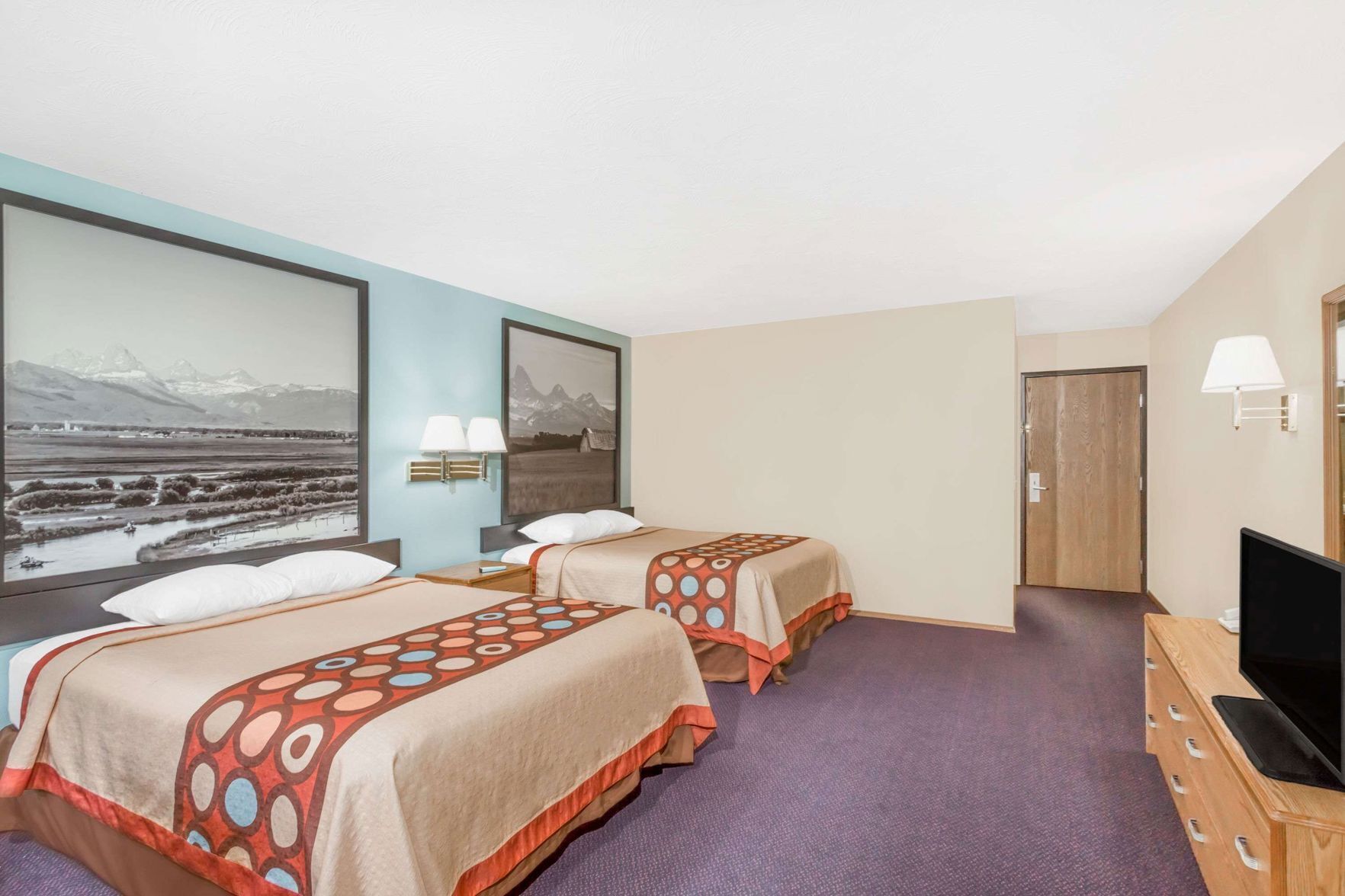 Een hotelkamer met twee bedden, een televisie, een bureau en een groot raam met uitzicht op de bergen.