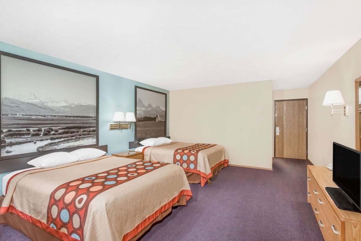 Een hotelkamer met twee bedden, een televisie, een bureau en een groot raam met uitzicht op de bergen.