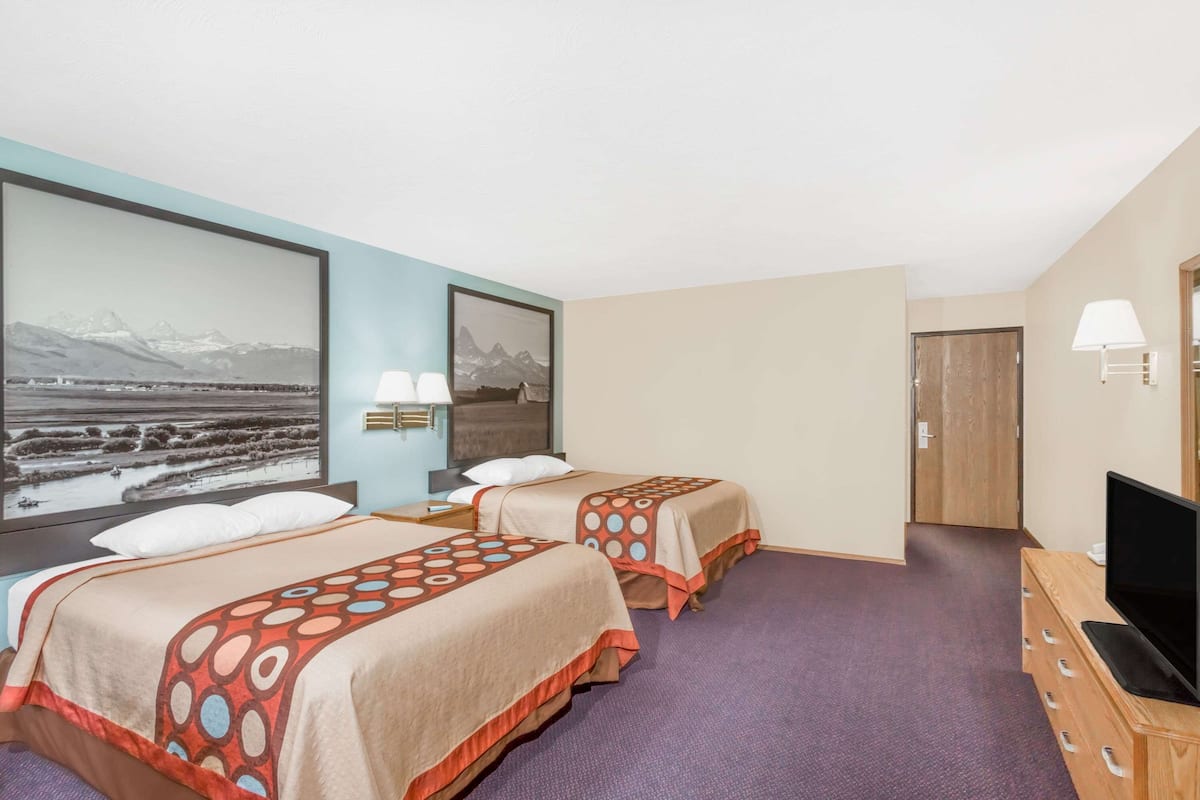 Een hotelkamer met twee bedden, een televisie en een groot ingelijst schilderij aan de muur.
