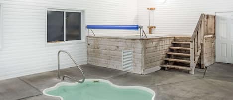 Un espacio reducido y cerrado con suelo de concreto, una piscina metálica, un banco de madera y una ventana.