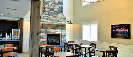 A cozy restaurant interior with a stone fireplace, wooden tables and chairs, and a chandelier.