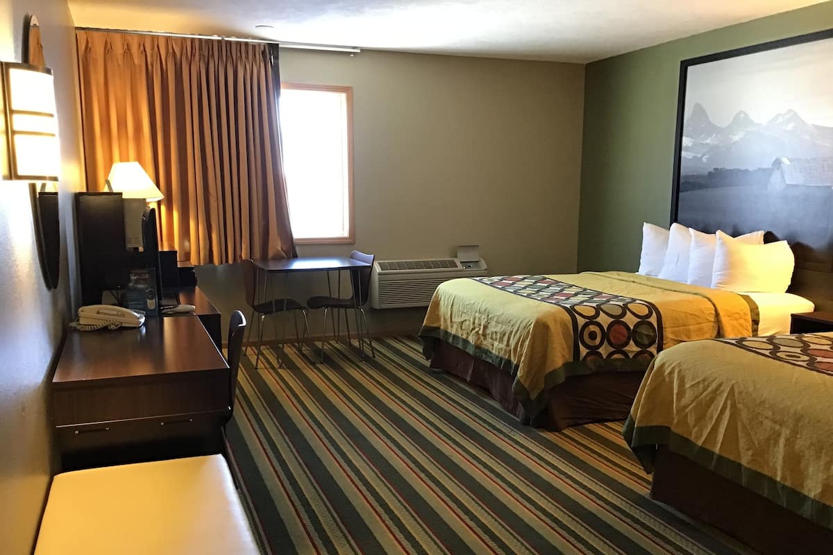 Een hotelkamer met een bed, bureau, stoel, telefoon en een raam met gordijnen.