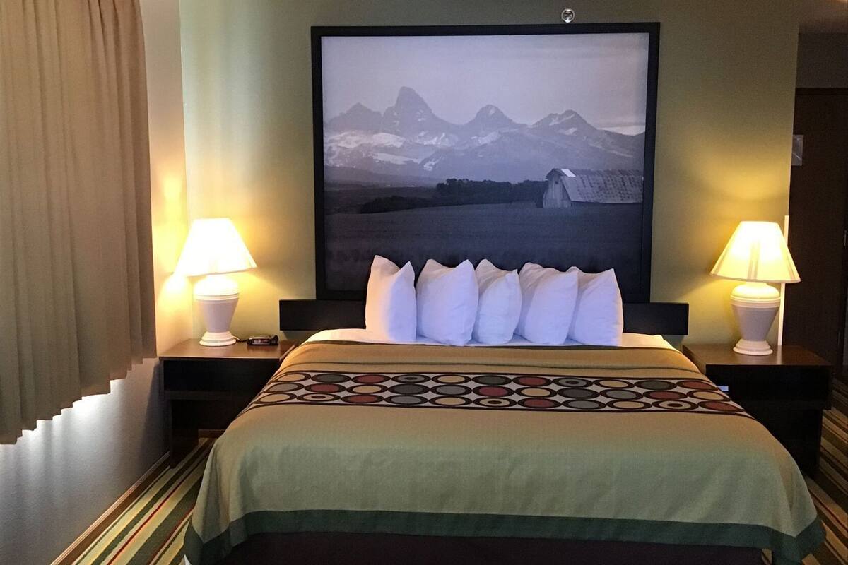 Een hotelkamer met een bed, twee bedlampen, een groot gepresenteerd schilderij aan de muur, en een gestreept tapijt.