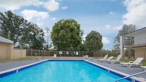 A swimming pool with a fenced deck area, lounge chairs, and a large tree in the background. - Super 8 by Wyndham Brinkley (Brinkley)