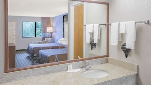 A hotel room with a large mirror, a bed with blue bedding, a bathroom with a sink and towel rack. - Super 8 by Wyndham Brinkley (Brinkley)