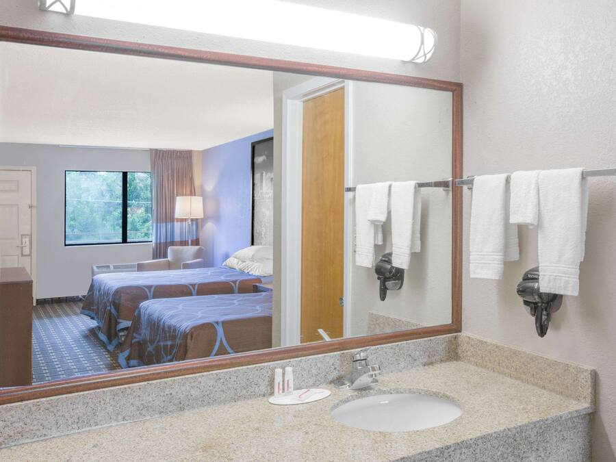 A hotel room with a large mirror, a bed with blue bedding, a bathroom with a sink and towel rack.