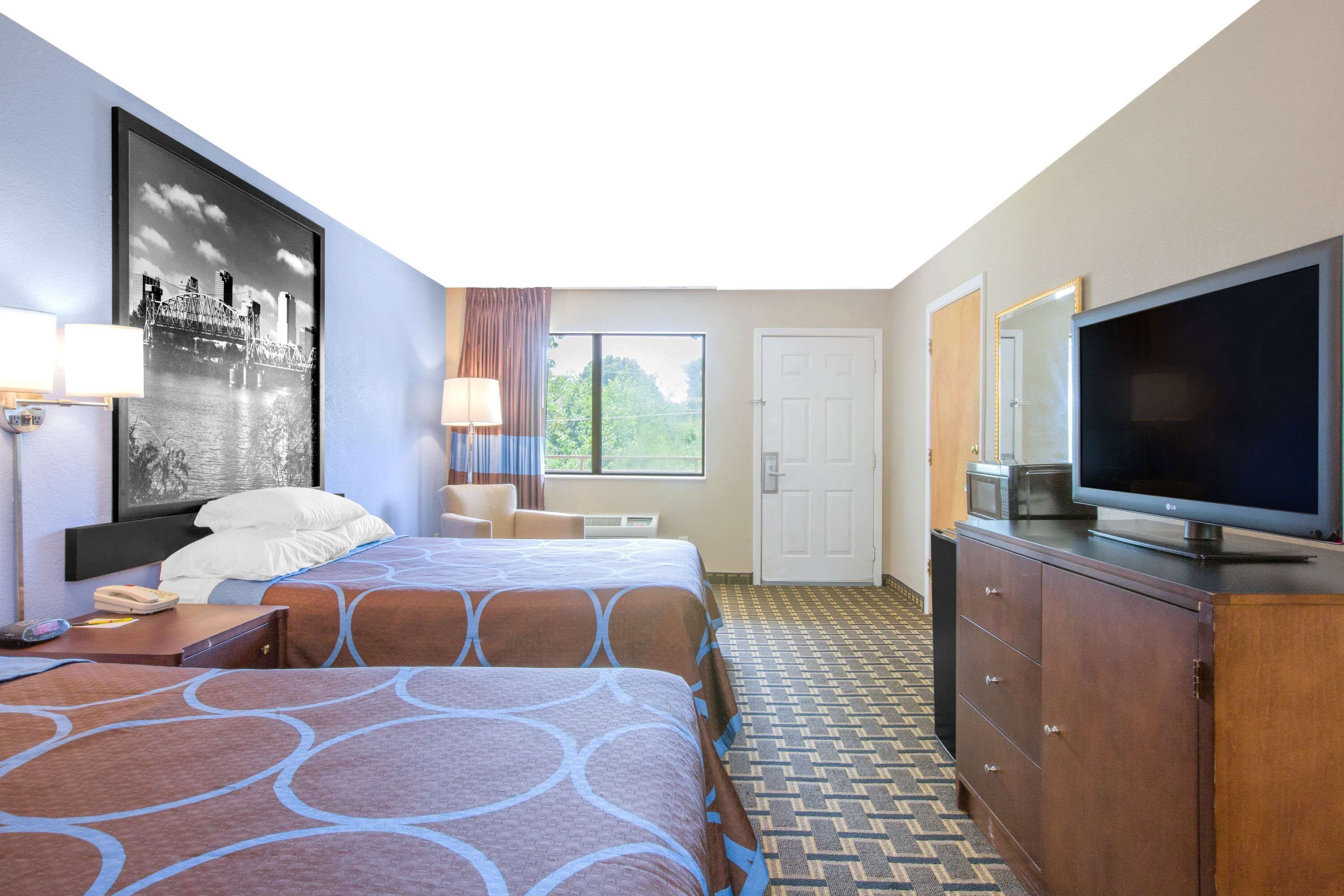 Een hotelkamer met twee bedden, een televisie, een bureau met lamp, een raam met gordijnen en een deur.