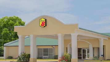 Welcome to our hotel, featuring a distinctive logo above the entrance and a green roof supported by white columns.