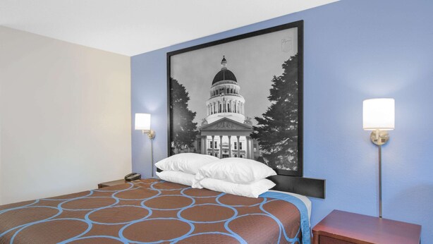 A hotel room with a large bed, a framed picture of a building on the wall, two bedside lamps, and a wooden nightstand. - Super 8 by Wyndham Brinkley (Brinkley)