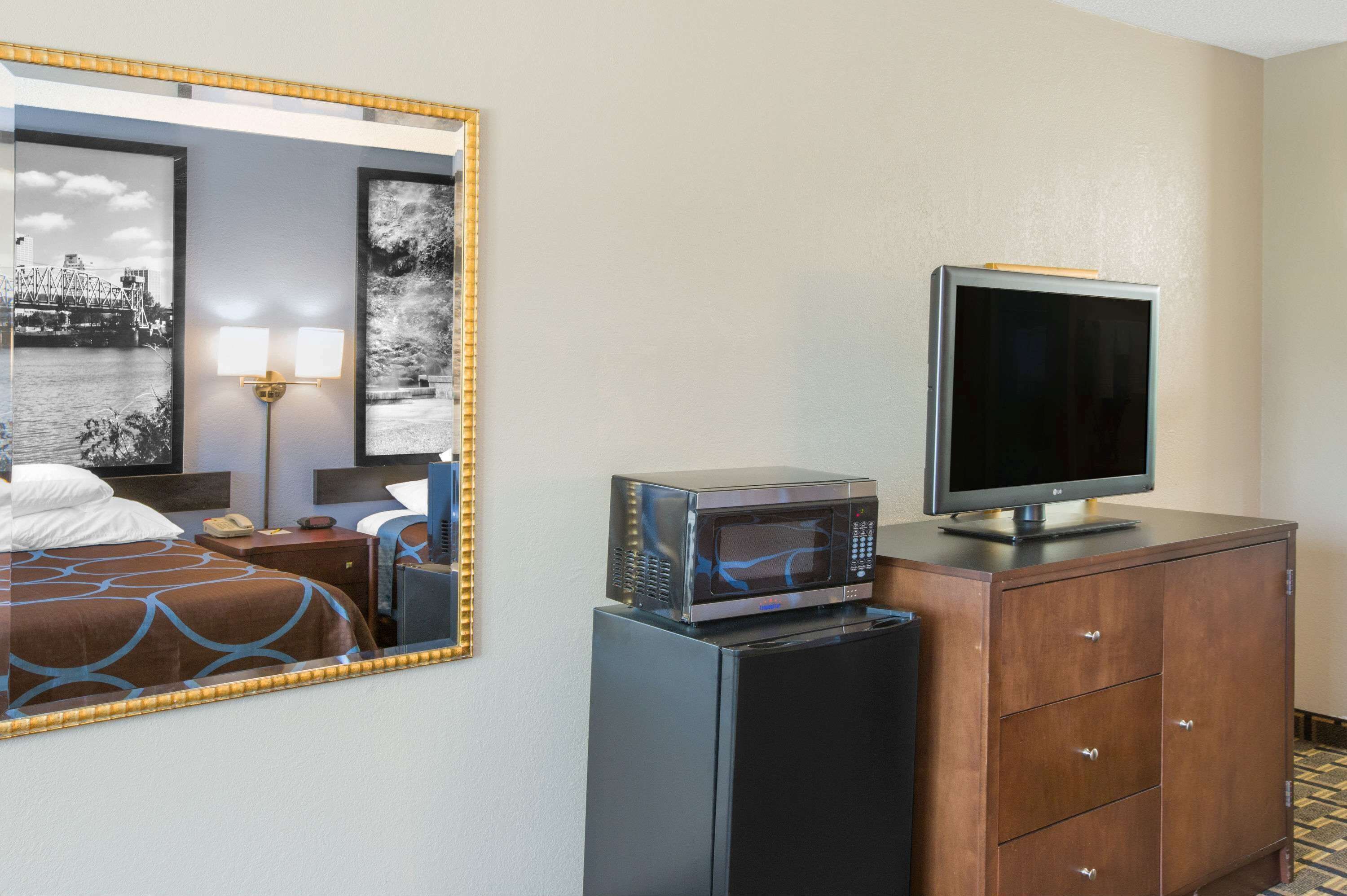 A hotel room with a bed, a desk with a lamp, a microwave, a television, and a cabinet.
