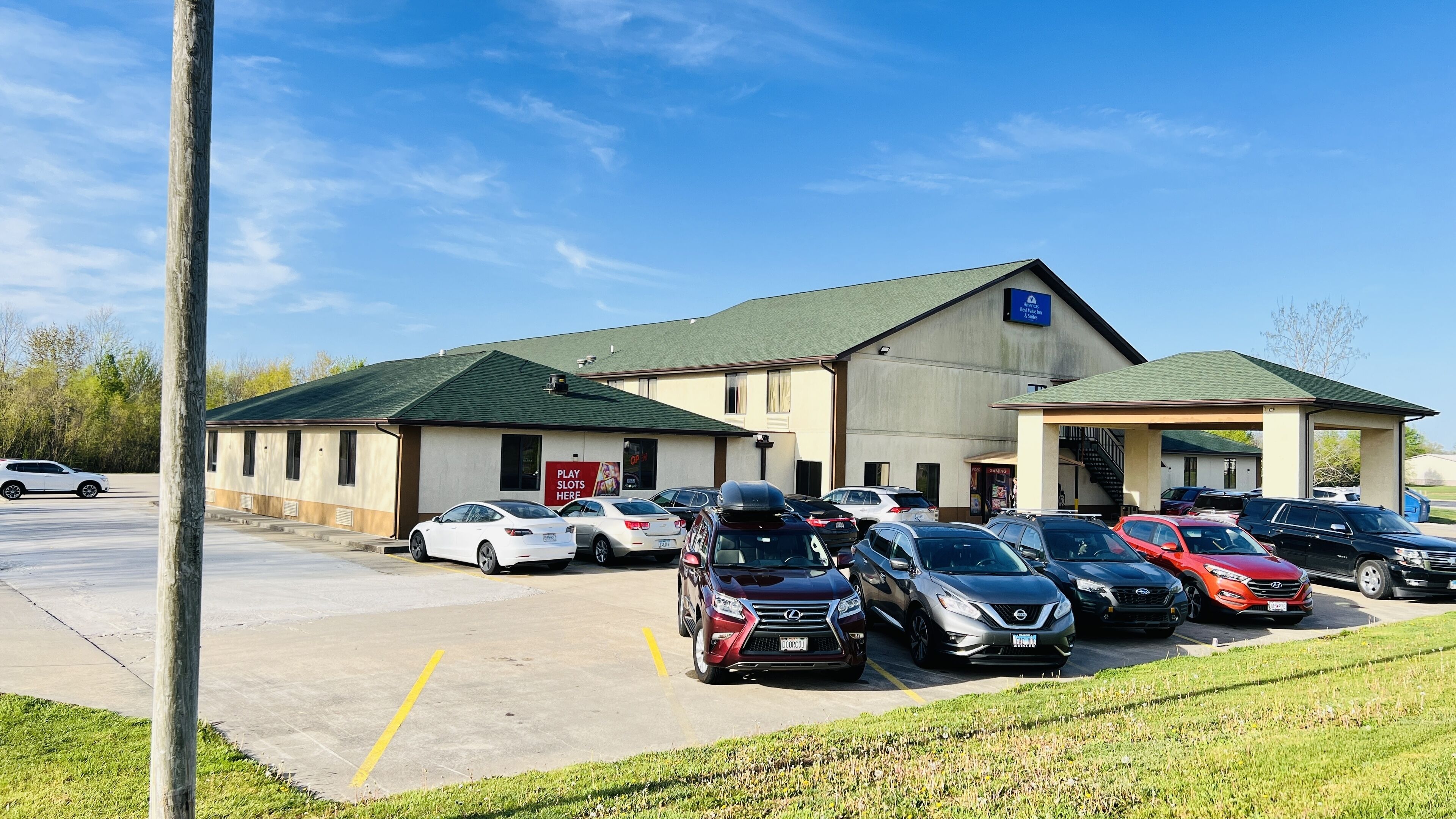A parking lot with multiple cars and a building with a green roof and a sign that reads "PLAY SLOTS HERE".