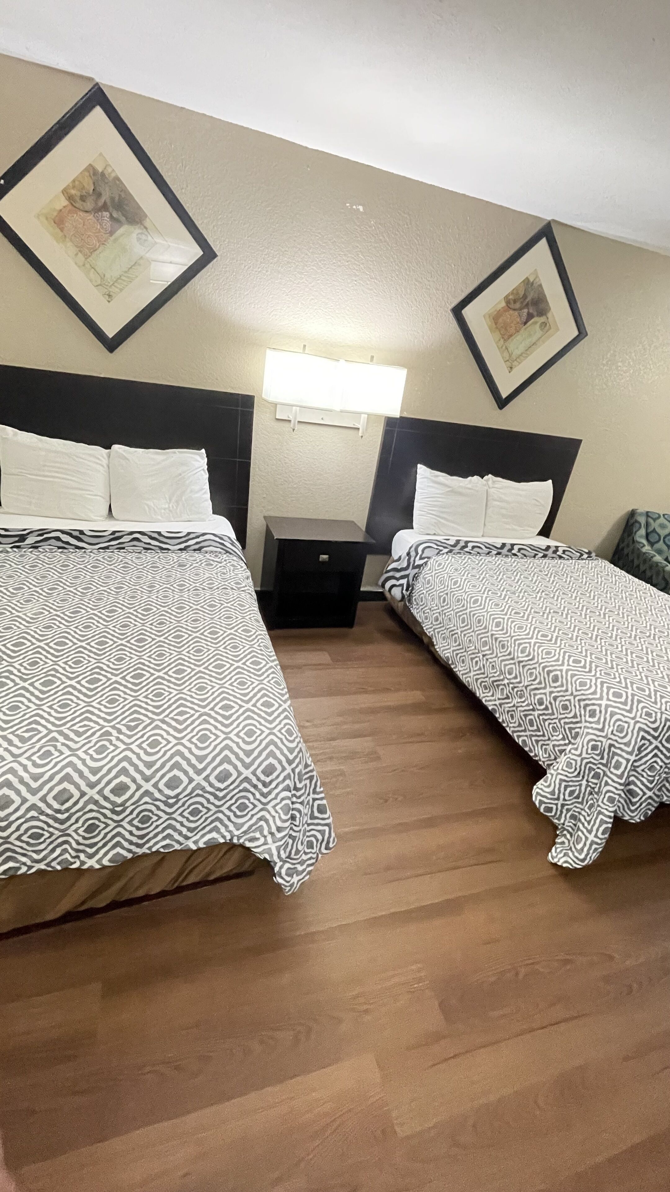 Habitación de hotel con dos camas, una mesita de noche, una lámpara de pared y cuadros en la pared.