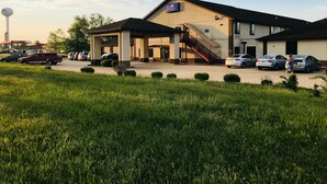 A hotel with a covered outdoor area, a staircase leading to the entrance, and a parking lot with several cars. -  Pinckeyville Inn and Suites (Pinckneyville)