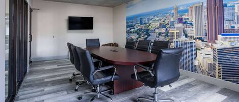 A conference room with a large table, six chairs, a flat-screen TV, and a cityscape mural on the wall.