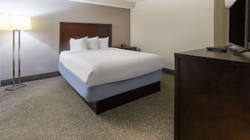 Una habitación de hotel con cama, mesita de noche, escritorio, lámpara y televisor.
