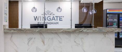 Bancada de recepção com tampos de mármore e uma placa indicando "Wingate by Wyndham".