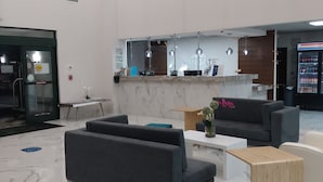 A modern lobby with marble flooring, a reception desk, seating area, and a vending machine.