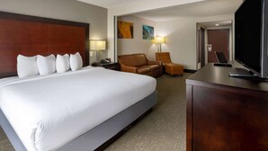 A hotel room with a large bed, a desk, a television, and a seating area with a chair and a sofa.