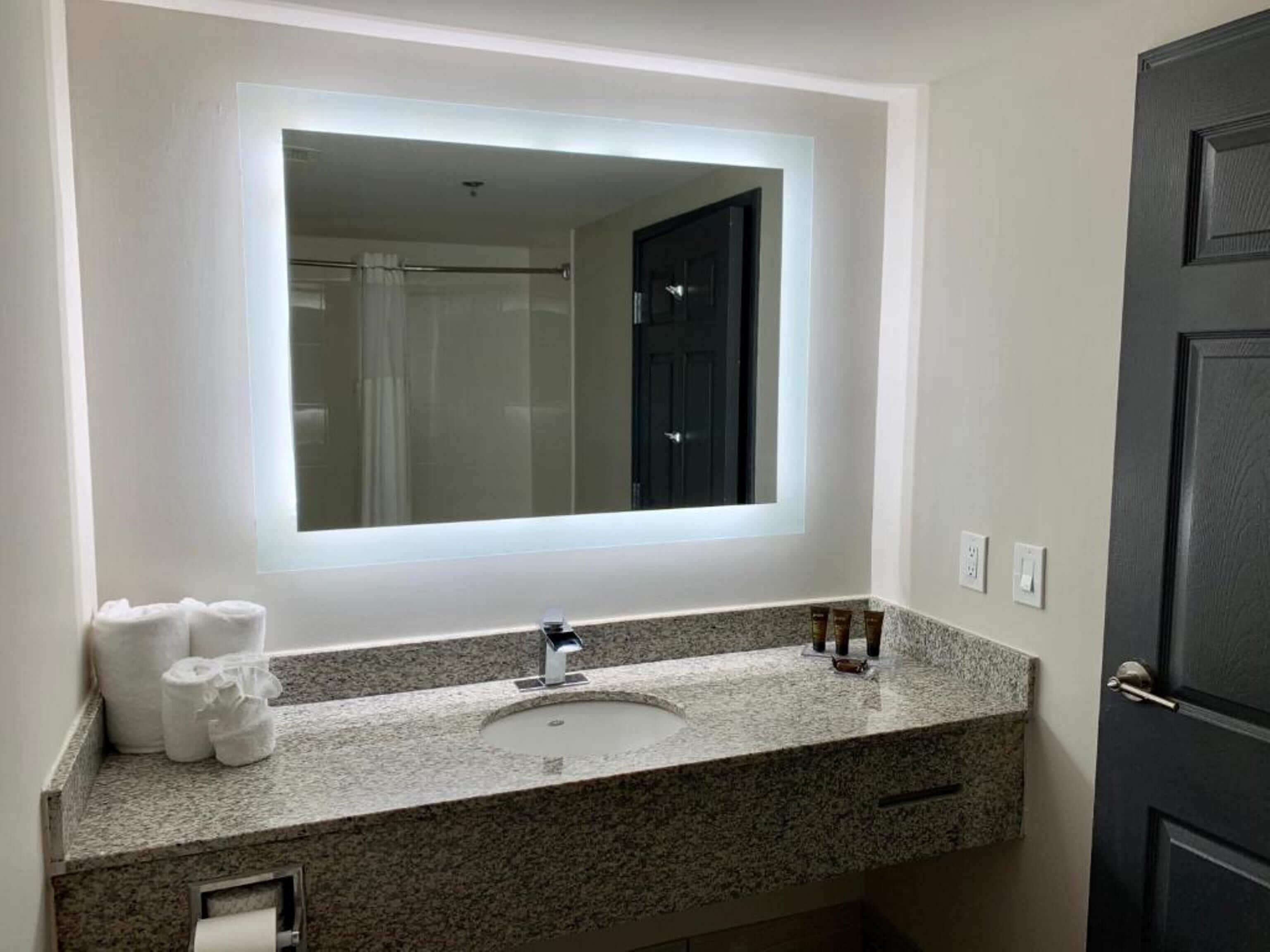 Un baño con encimera de granito, un lavabo, un espejo y una puerta.