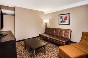 A hotel room with a brown leather sofa, a matching ottoman, a small table, a lamp, and a framed abstract painting on the wall.