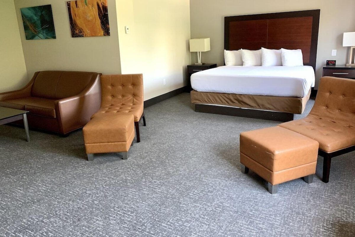 A hotel room with a large bed, two armchairs, a small table, and artwork on the walls.