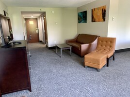 Una habitación de hotel con un escritorio, un sofá de cuero marrón, una mesita y dos cuadros en la pared.