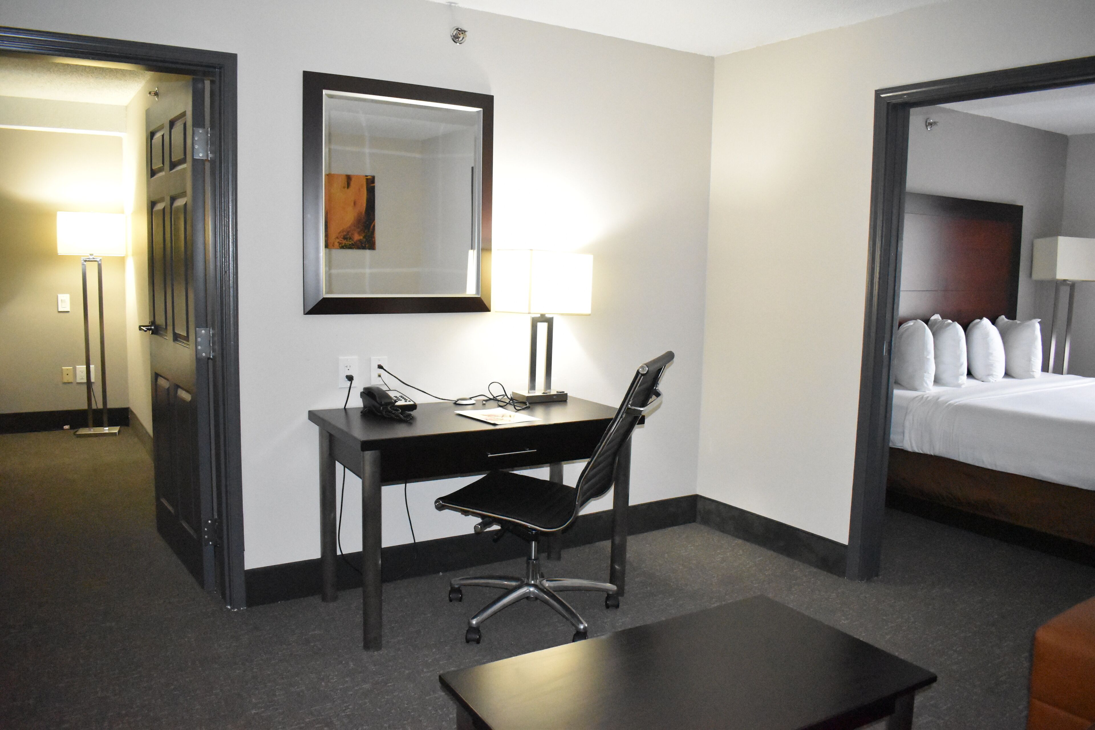 A hotel room with a desk, chair, and a bed with pillows.