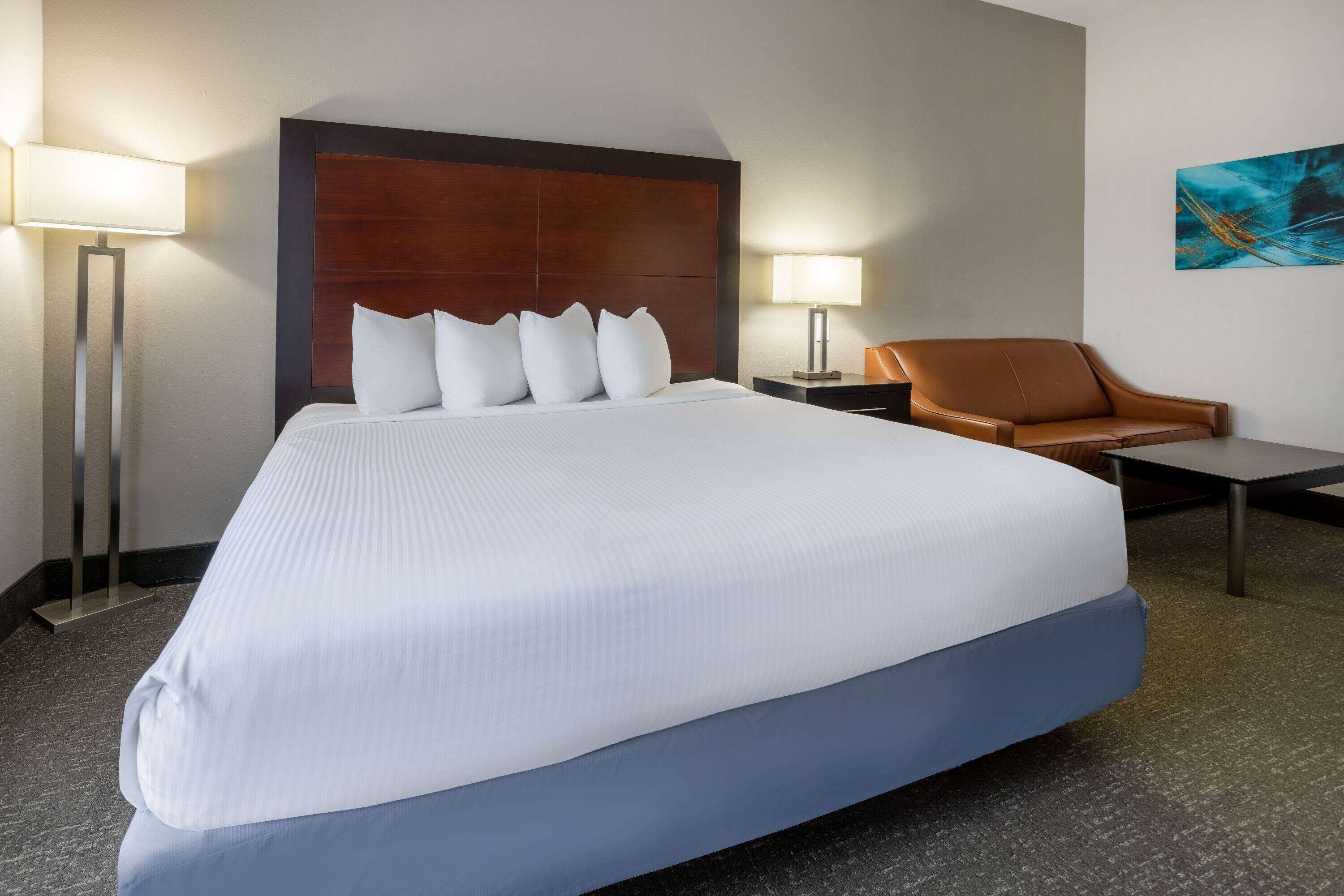 A hotel room with a large bed, a brown leather chair, a small table, and two bedside lamps.