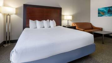 Una habitación de hotel con una cama grande, un sillón de cuero marrón, una mesita pequeña y dos lámparas de noche.