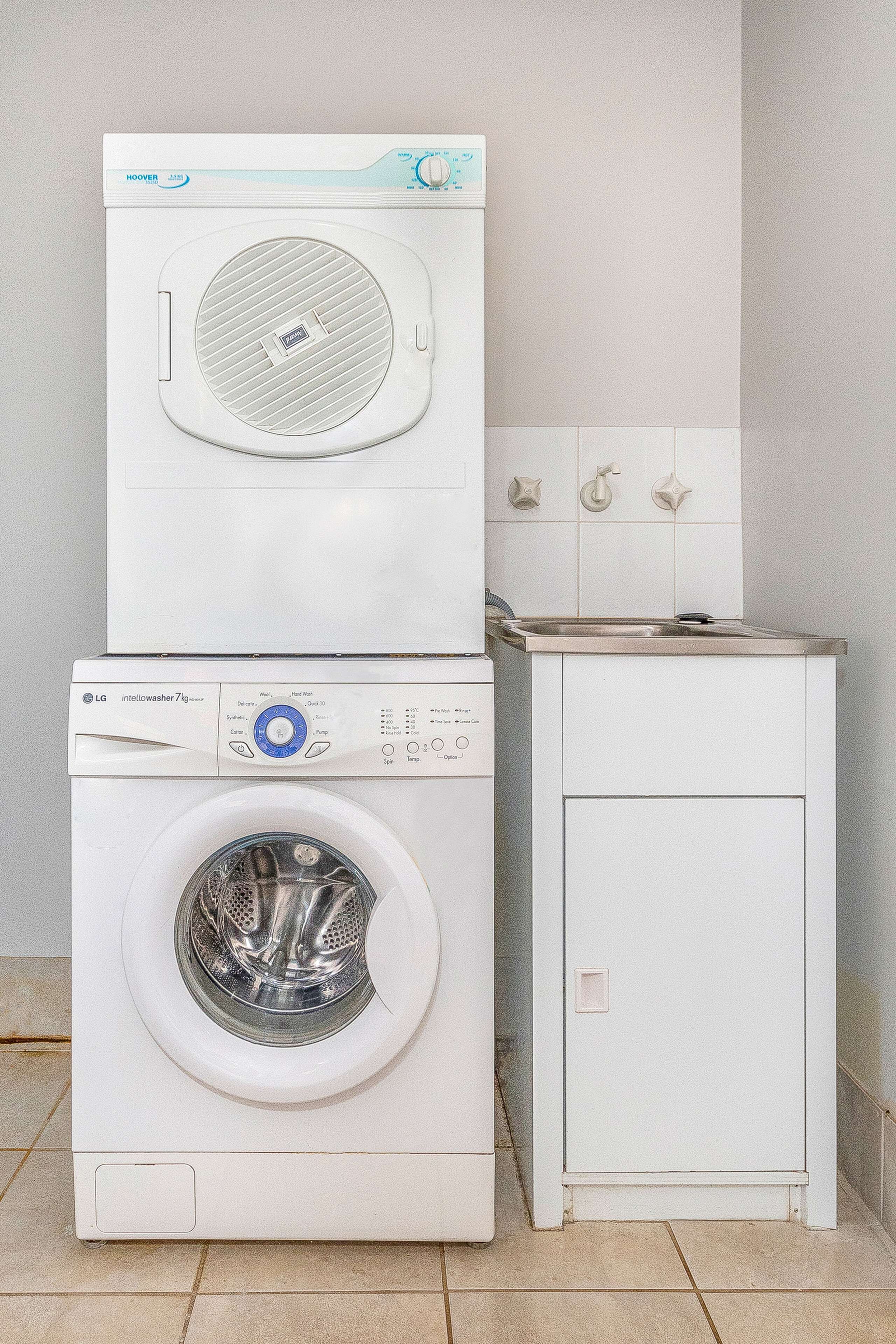 Een gestapelde wasmachine en droger met een klein kastje eronder.