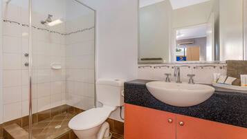 A bathroom with a glass shower enclosure, a white toilet, a sink with a granite countertop, and a mirror above the sink.