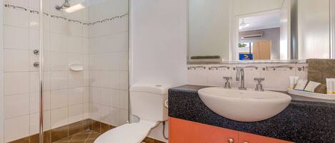 Une salle de bain avec une douche à parois de verre, des toilettes blanches, un lavabo avec un plan de travail en granit et un miroir au-dessus du lavabo.