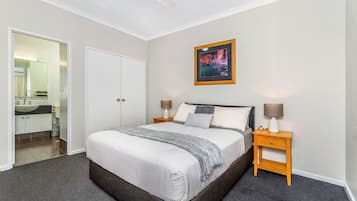 A bedroom with a large bed, two bedside tables with lamps, a framed picture on the wall, and a door leading to a bathroom.